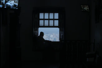 Silhouette of a thoughtful woman gazing into a dimly lit room with digital code flowing softly around her.