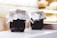 Two jars filled with dark contents are placed on a light-colored surface against a brick background. Each jar has a fabric cover secured with twine and a label featuring Russian text and a wheat graphic.