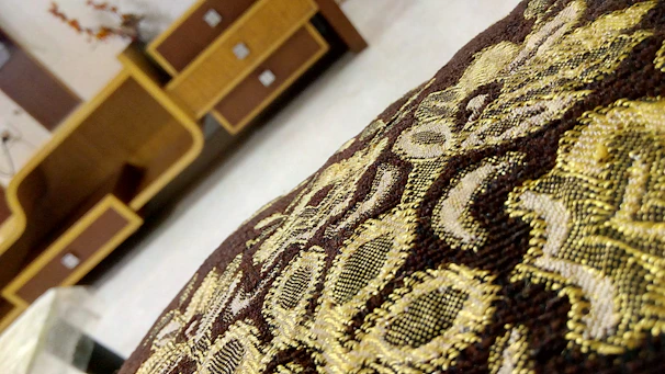 Close-up of a delicate embroidered kufi resting on a wooden table beside a folded kamis.