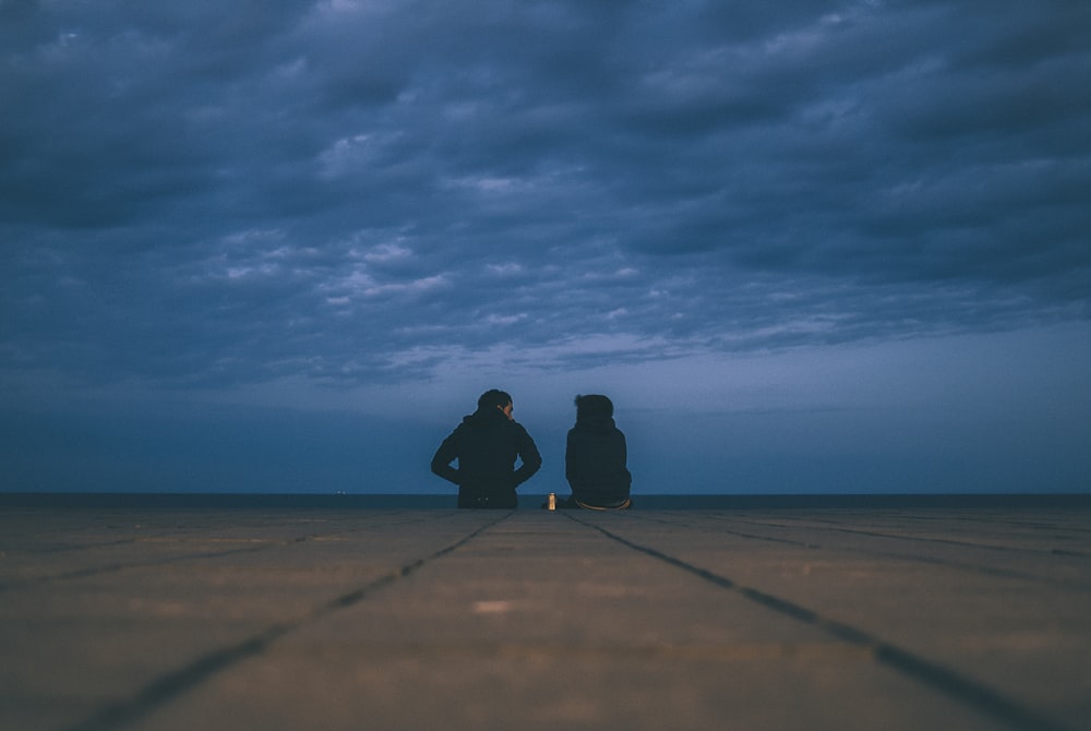 two people wearing black jackets sitting on floor