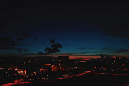 A dramatic cityscape at dusk captured by a drone, with cinematic color grading and glowing silver UI overlays.