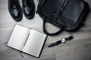 A journal open with handwritten notes and a pair of running shoes beside it on a wooden floor.