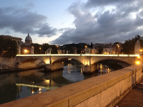 High-contrast shot of an ancient stone bridge over a dark river at dusk.