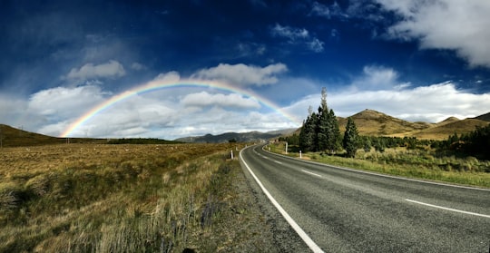 highway near trees and rainbow under blue sky in Tekapo New Zealand