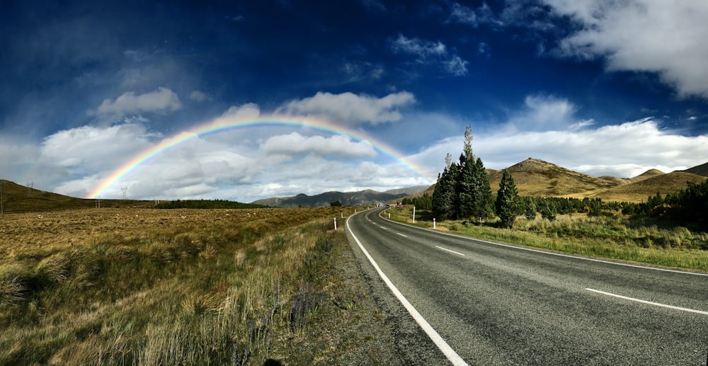 Autobahn in der Nähe von Bäumen und Regenbogen unter blauem Himmel