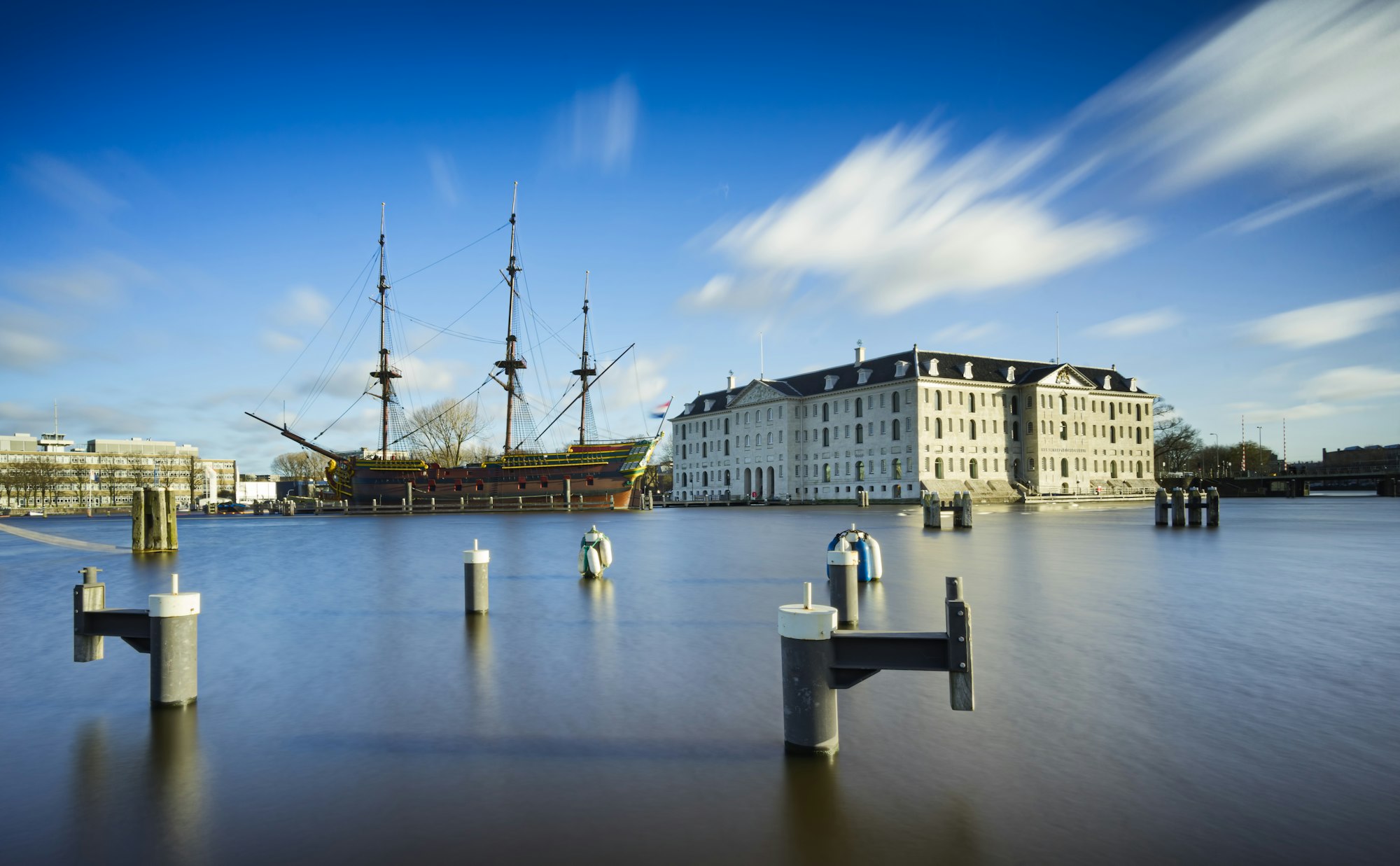 Maritime scene with pilings in foreground, colonial architecture, and sailing ship.