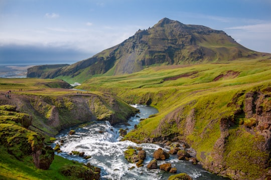photo of river and green grass covered moutain in Skógafoss Iceland