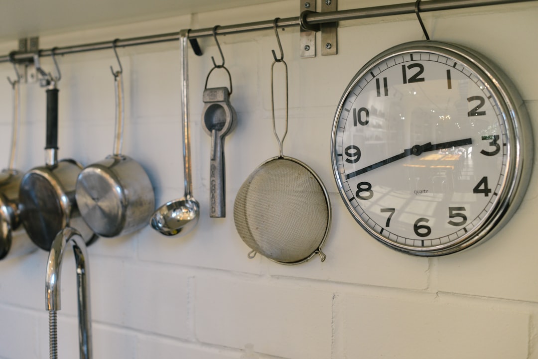 round white and gray stainless steel analog clock displaying 02:43 time near gray stainless steel saucepans hanging on wall