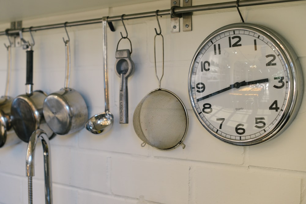 round white and gray stainless steel analog clock displaying 02:43 time near gray stainless steel saucepans hanging on wall