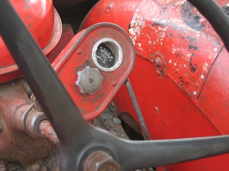 A close-up view of a vintage red tractor with a worn-out surface. The image captures a part of the steering wheel, a round gauge with black and white readings, and a metal knob.