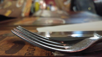 A close-up of a beautifully crafted stainless steel fork resting on a rustic wooden table.