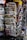 A rack filled with a variety of newspapers and magazines, featuring multiple languages and diverse topics. The publications are neatly arranged in several tiers, showcasing different headlines and imagery. The setting appears to be a newsstand, possibly located in a public area with other items partially visible in the background.