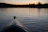 A serene Finnish lake at sunset with a kayak gliding across the water.