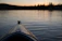 A serene Finnish lake at sunset with a kayak gliding across the water.