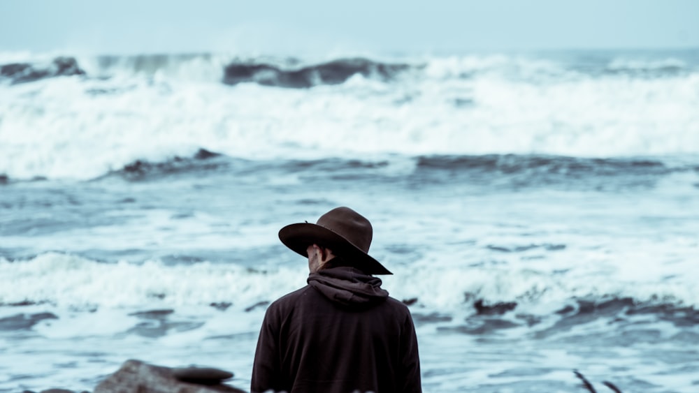 man wearing brown hat standing in front of ocean