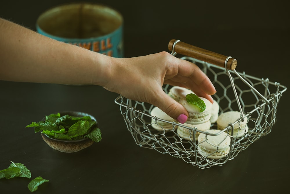 person holding round cookie near green leaf vegetable