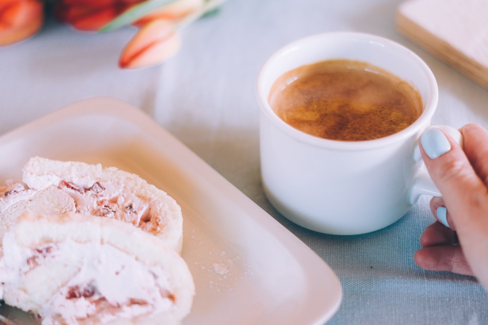 white mug filled with brown liquid beside tray with pastry