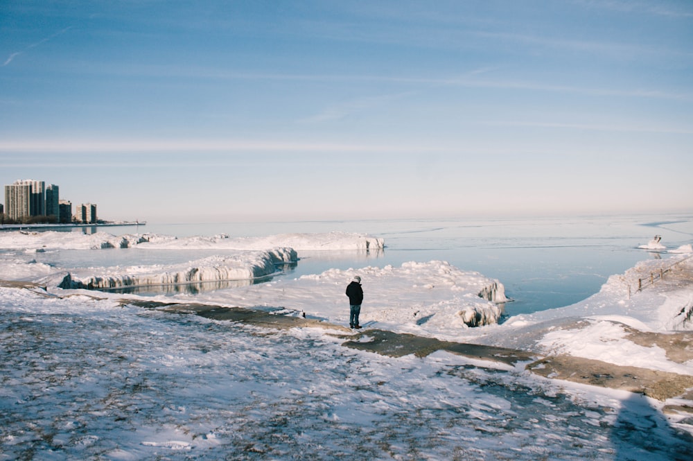 man stands between snowfield near body of water