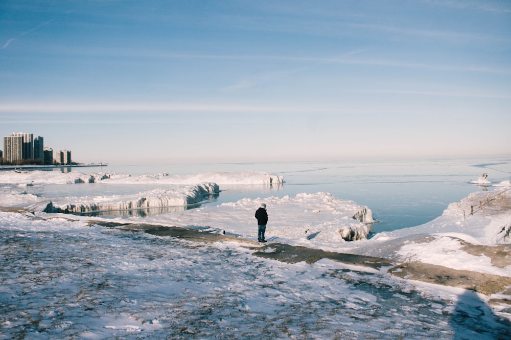 Un homme se tient entre un champ de neige près d’un plan d’eau