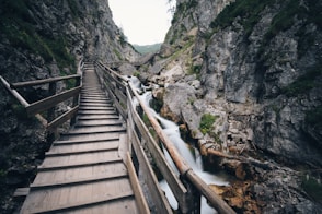 brown wooden bridge in the middle of two mountain