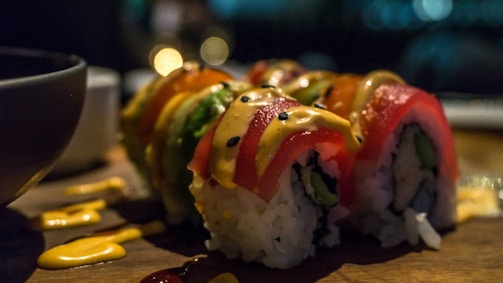 Close-up of colorful dulce sushi rolls arranged on a rustic wooden board with fresh strawberries and edible flowers.