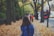woman with blue backpack on street full of fallen leaves