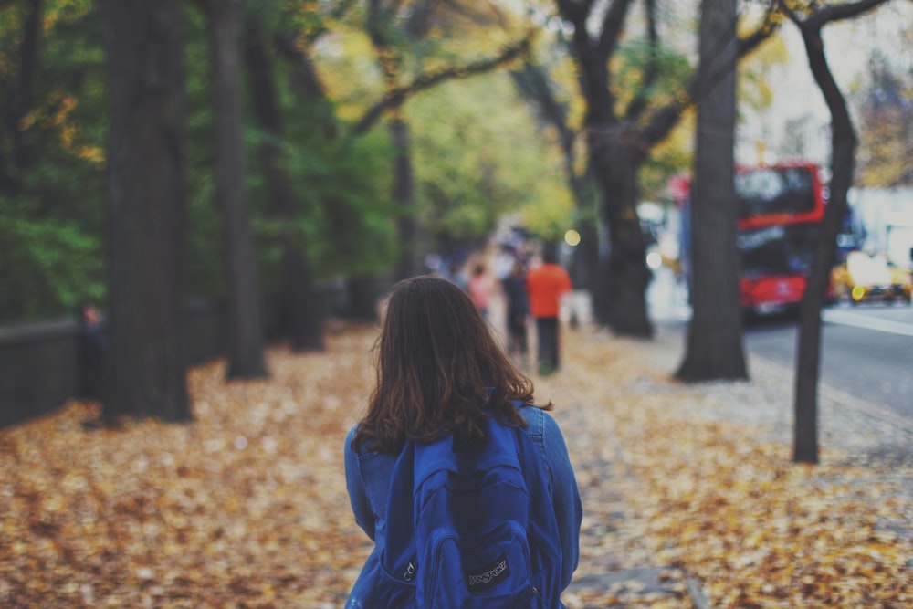 Frau mit blauem Rucksack auf der Straße voller heruntergefallener Blätter