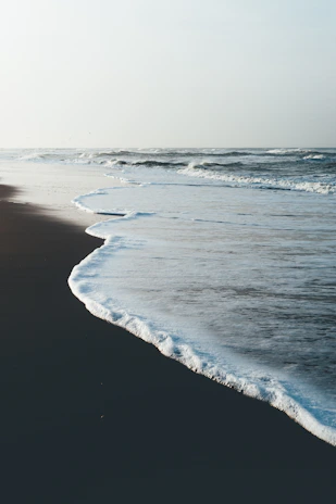 A calm coastal scene with gentle waves and a pale blue horizon.
