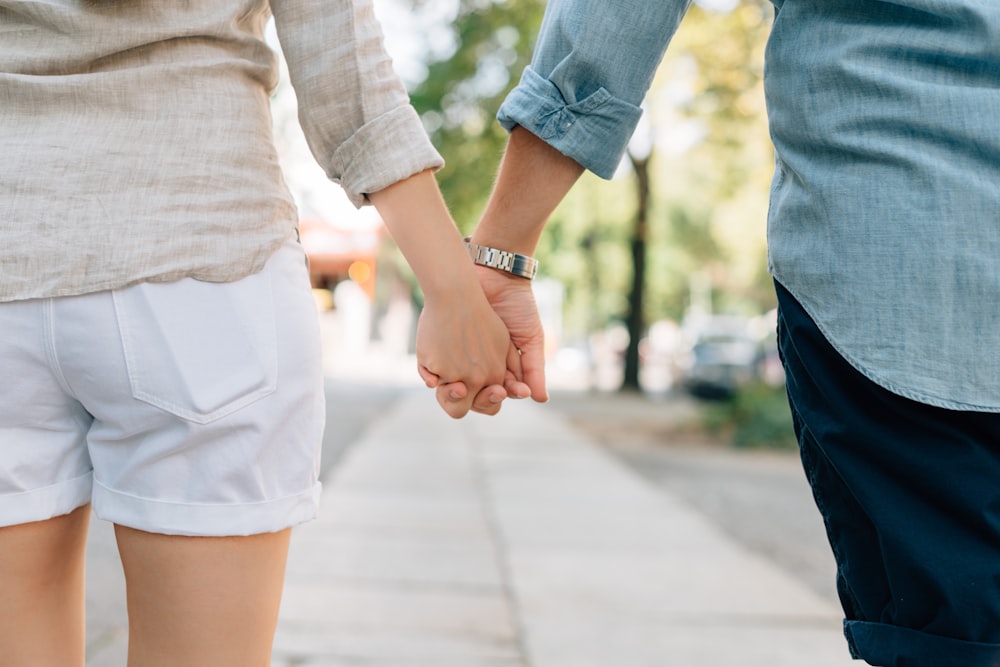 Mann und Frau, die tagsüber auf dem Gehweg Händchen halten