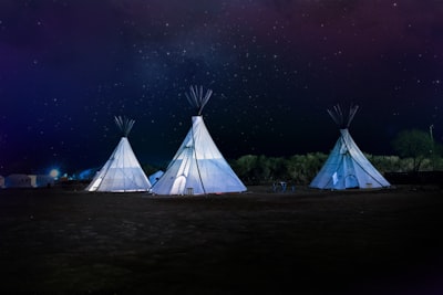 three white teepee tents under starry sky native teams background