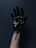 A hand covered in a glossy, viscous black substance, possibly paint or oil, against a dark background. The substance is dripping down the wrist.