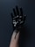 A hand covered in a glossy, viscous black substance, possibly paint or oil, against a dark background. The substance is dripping down the wrist.
