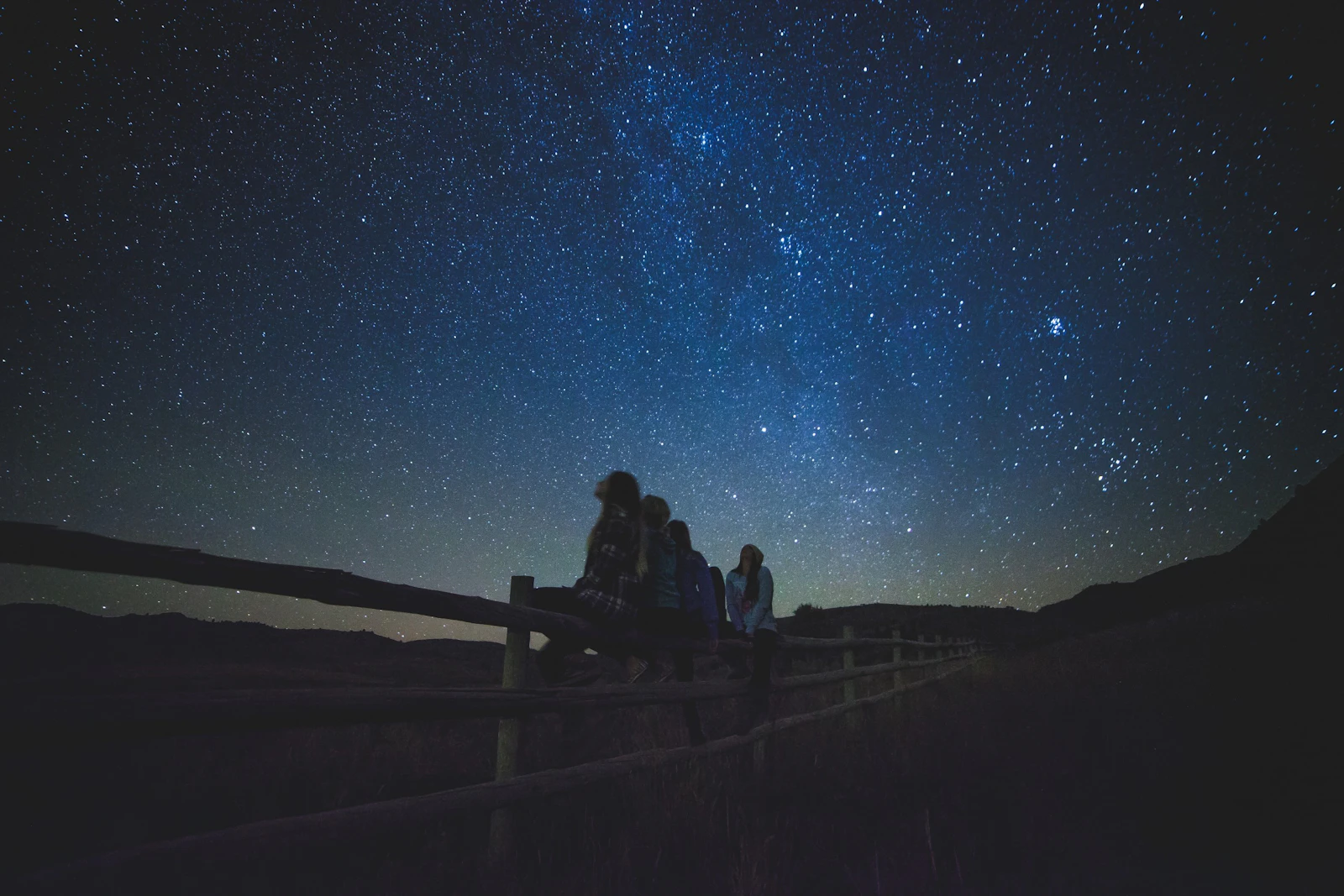 Several people sitting together outside at night under the Milky Way