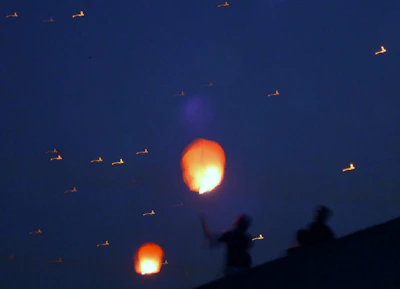 Color smoke and sky lanterns drifting into the evening sky at a festive wedding event.