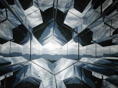 A hexagonal tunnel of mirrors reflecting a distant mountain range under a cloudy sky