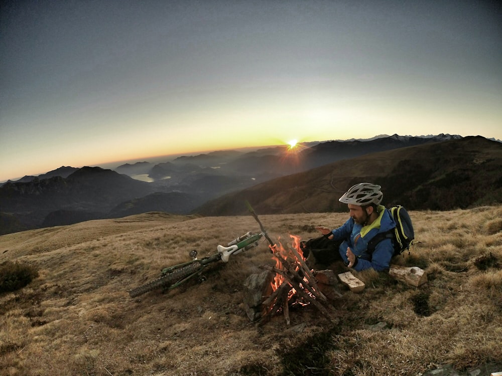 Mann liegt bei Sonnenaufgang auf braunem Gras vor Knochenfeuer