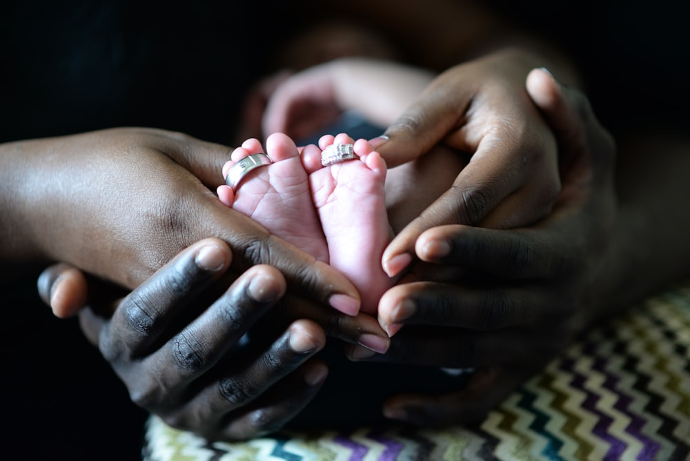 person touching baby's feet with two silver-colored rings