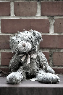 An antique teddy bear with worn fur and a patched ear resting against a stack of old books.