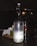 A translucent glass bottle prominently displays a label indicating it contains pure still water. Next to the bottle, a glass with a lit candle inside casts a warm light, creating a cozy ambiance. The background features subtle reflections and shadows, suggesting a dimly lit setting.