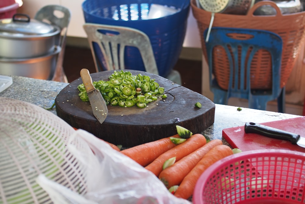 茶色の木製のまな板にベージュの包丁の近くに緑の野菜