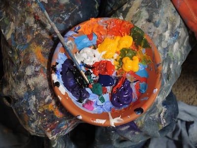paintbrush in a brown clay bowl with small amounts of paints of different colors, yellow, blue, white, orange, blue and greeen