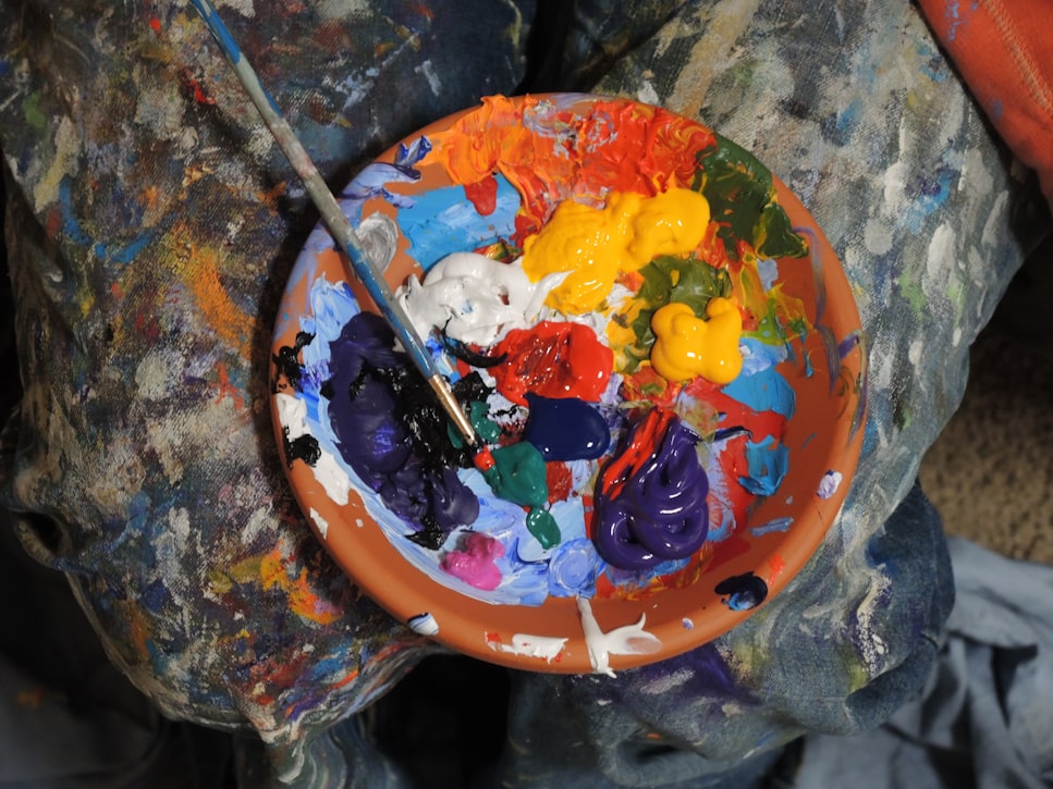 Mix of paints in a orange bowl with paintbrush sit on a messy background