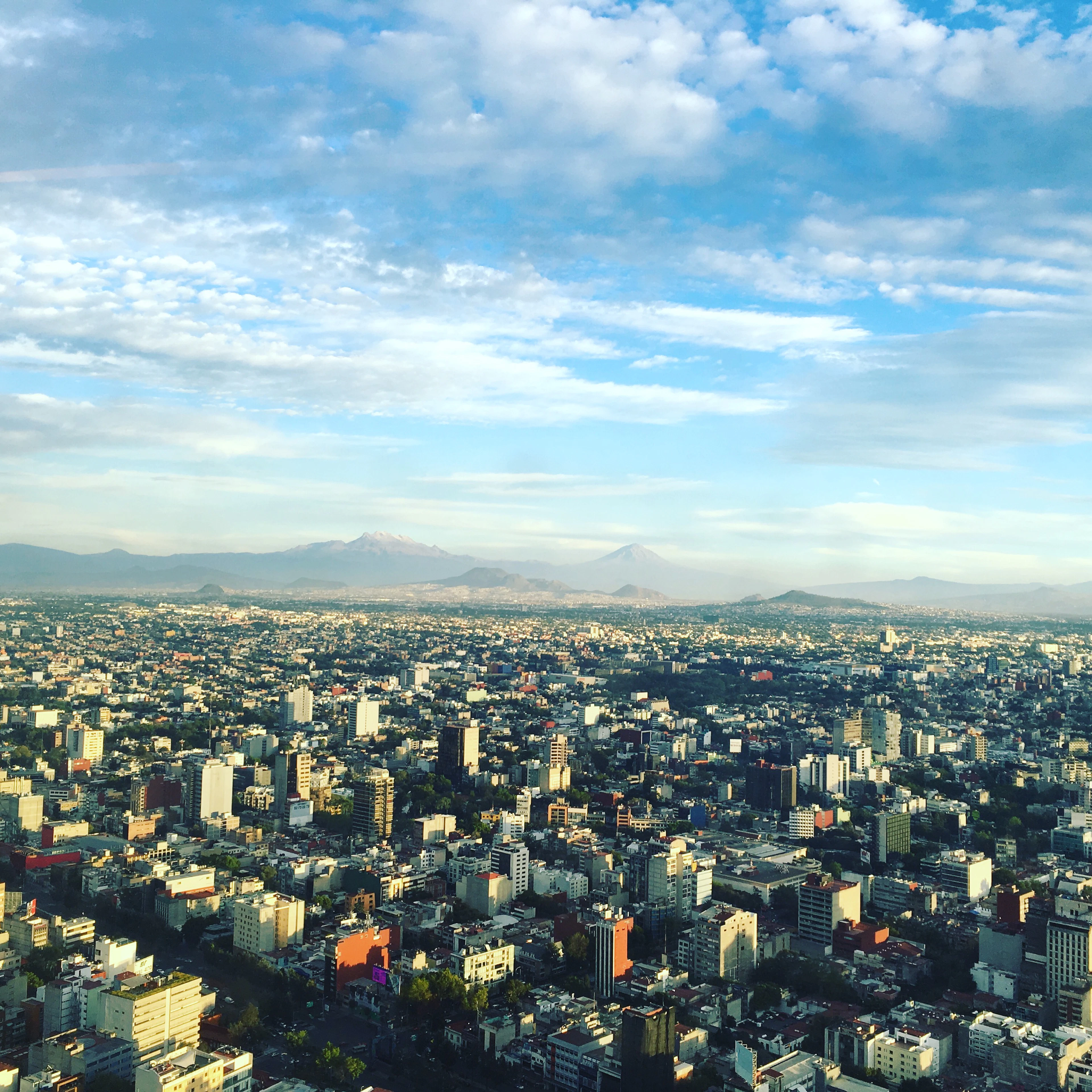 An aerial view of Mexico City's dense sprawl stretching toward distant mountains in warm morning light.