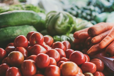 red tomato beside pile of orange carrots close-up photo produce teams background