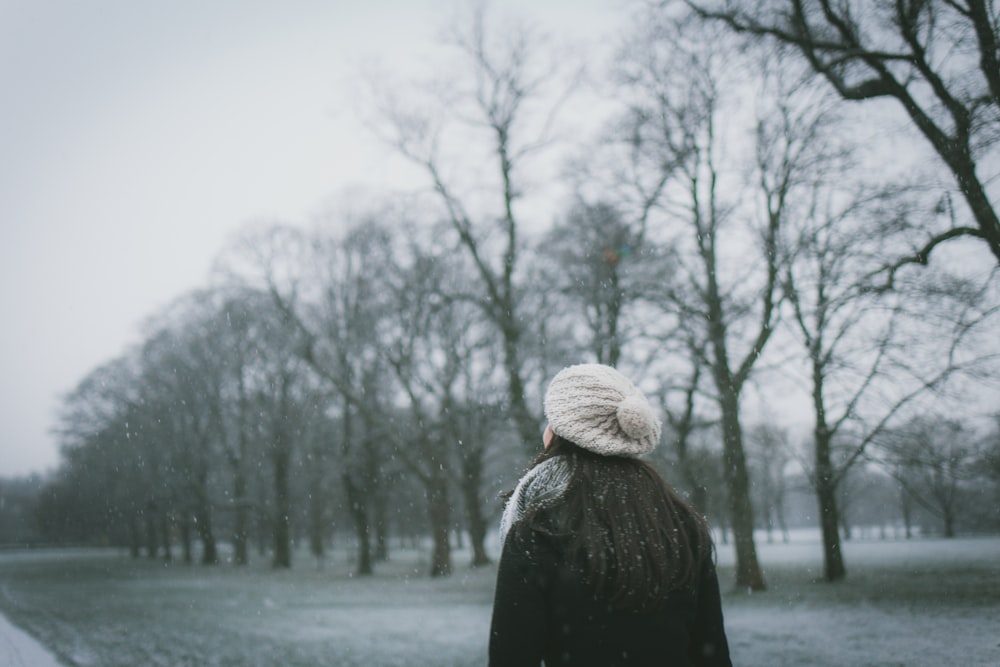 Femme portant une casquette et un manteau noir debout près d’un arbre nu