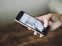 A hand holding a smartphone displaying a social media app, with a blurred background.