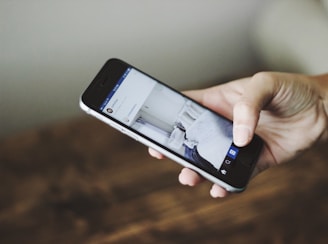 A hand holding a smartphone displaying a social media app, with a blurred background.