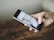 A hand holding a smartphone displaying a social media app, with a blurred background.
