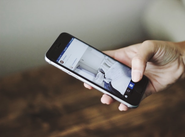 A hand holding a smartphone displaying a social media app, with a blurred background.