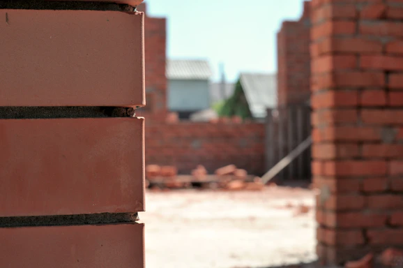 A close-up of hands laying bricks on a sunny construction site.